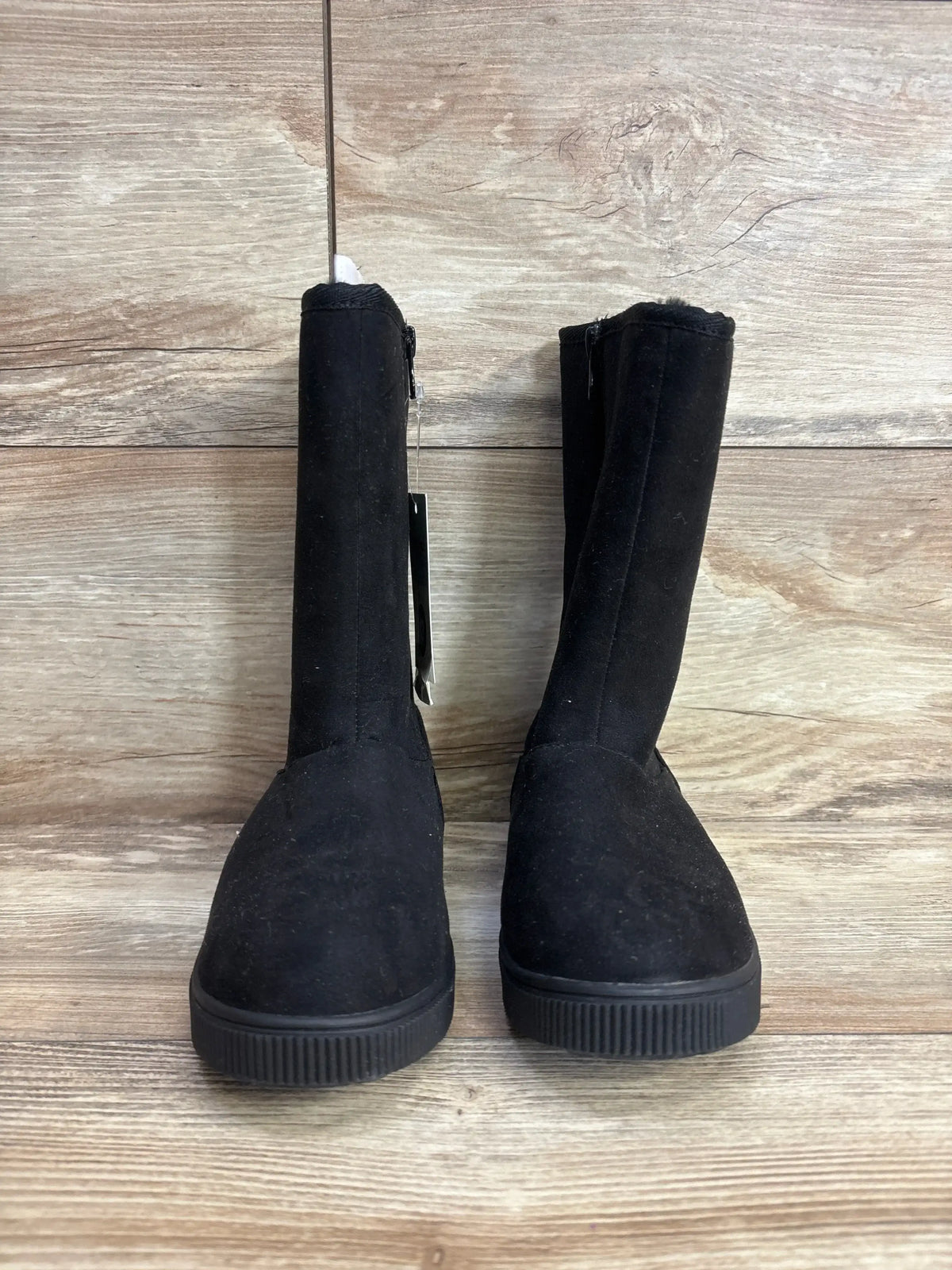 Pair of black suede children's boots with rubber soles on wood background