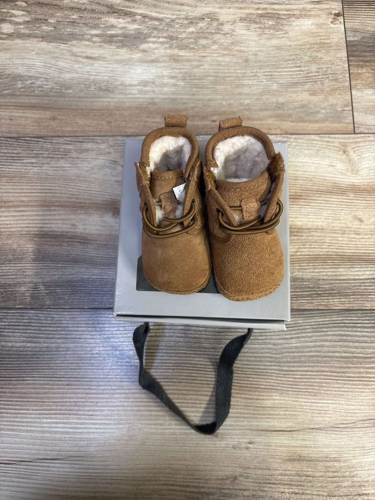 Top-down view of UGG Baby Neumel chestnut suede booties size 0/1C showing shearling lining and laces on gray box