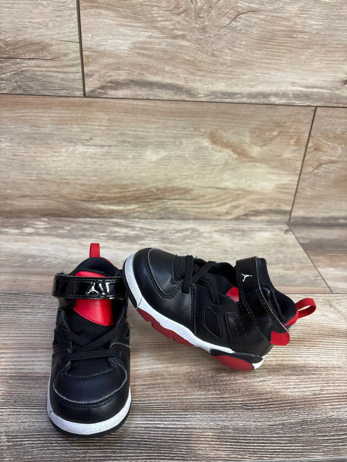 Angled view of Air Jordan Flight Club 91 TD sneakers showing black leather, red accents and white midsole on wood floor