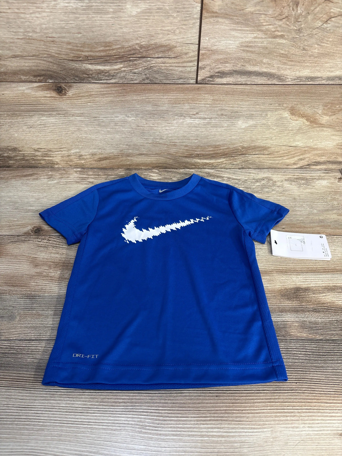 Front view of Nike Dri-Fit shirt in Game Royal Blue size 3T with white swoosh and short sleeves on wood background