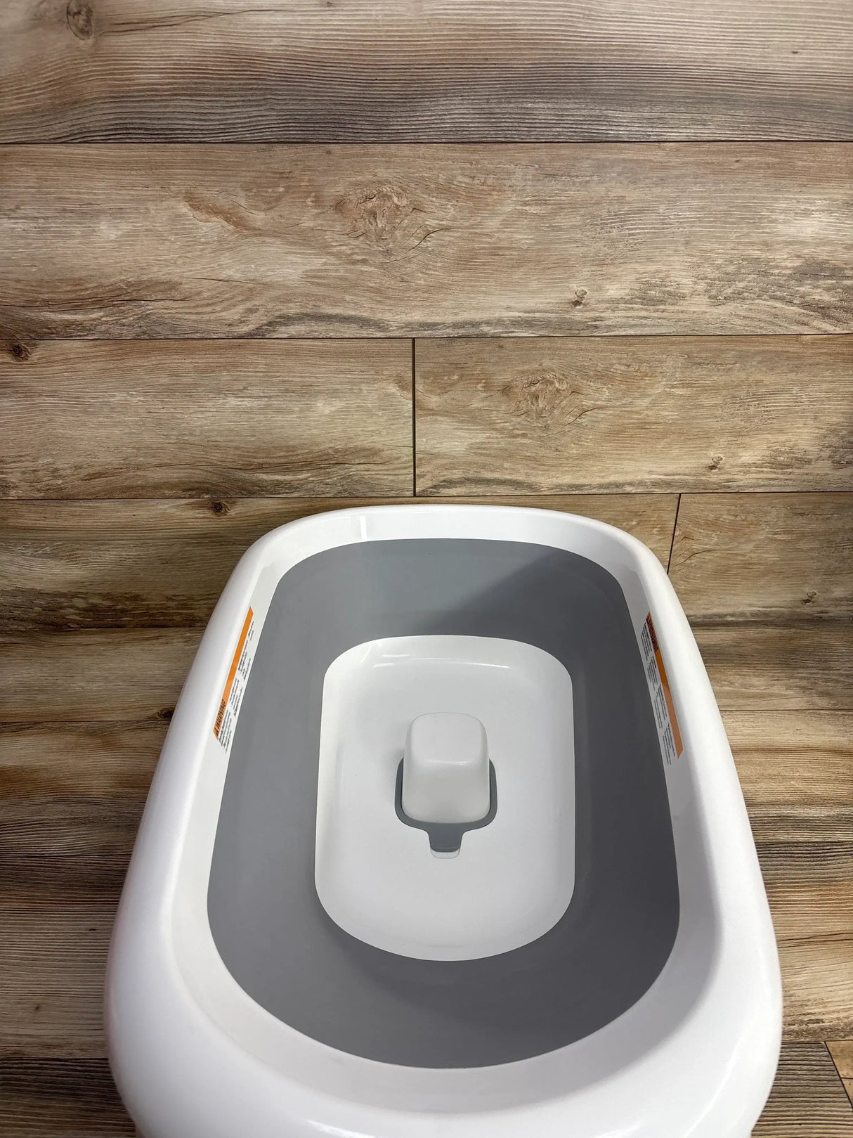 Top-down view of OXO Tot Splash & Store bathtub in grey showing built-in infant support and grey non-slip interior on wood plank background