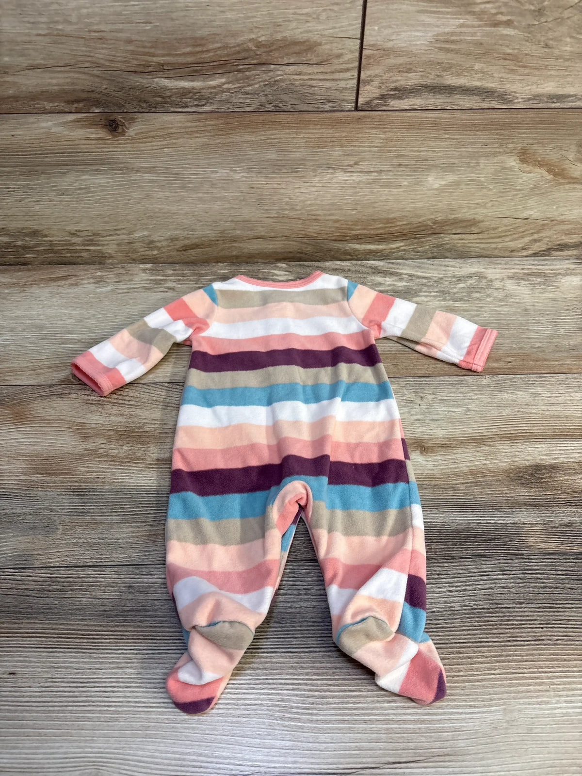 Flat lay of Carter’s newborn striped footed blanket sleeper showing multicolor horizontal stripes in pink, teal, cream and burgundy on a wood floor background