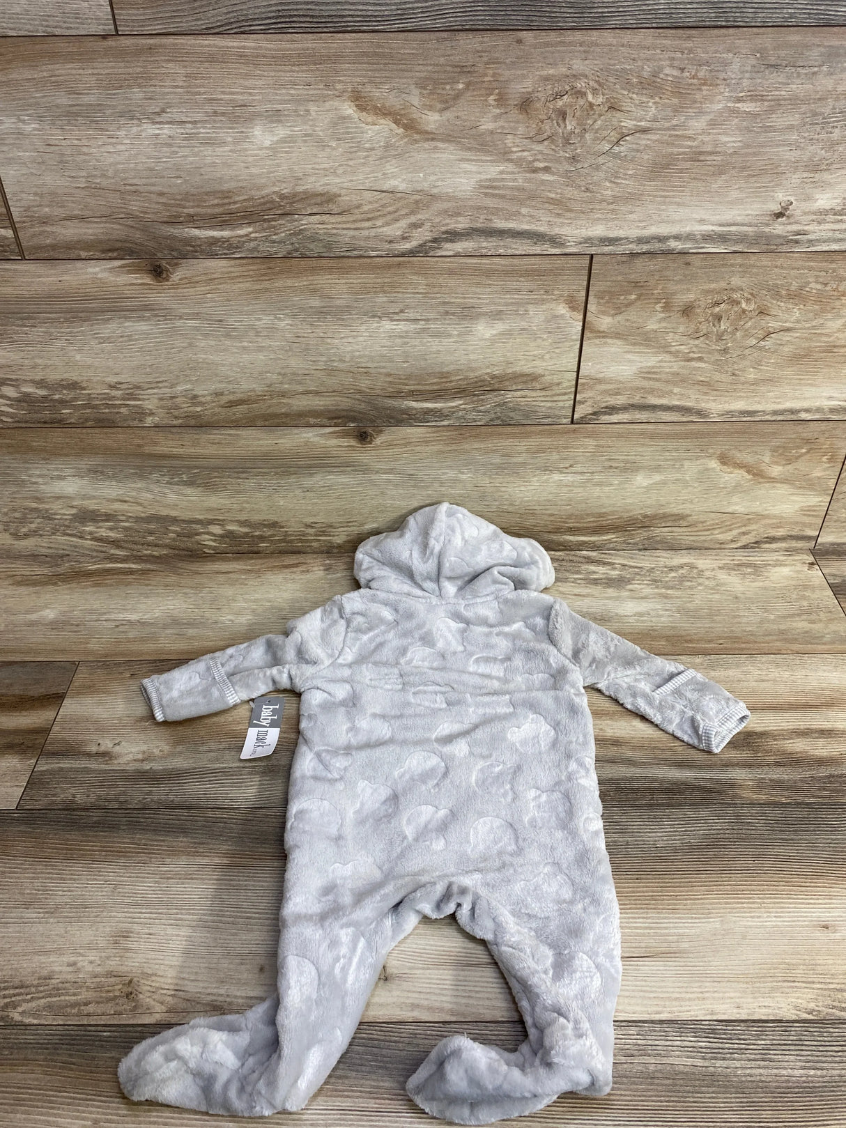 Gray plush baby onesie with hood and footed legs, textured with heart shapes, laid on wood floor