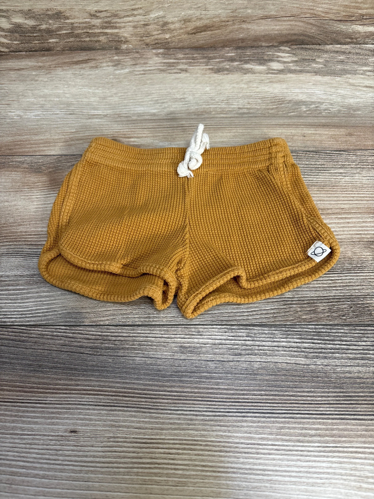 Flat-lay front view of My Little Cozmo organic waffle-knit baby shorts in oil yellow showcasing drawstring waistband on wood background