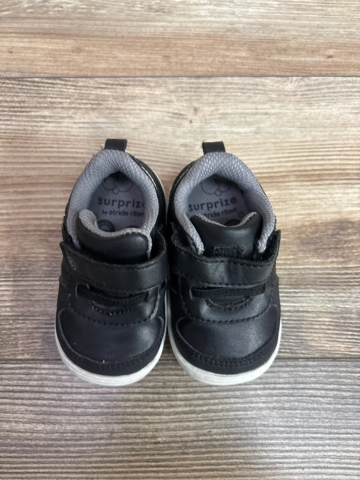 Top view of Surprize by Stride Rite black toddler sneakers size 3C with Velcro straps, gray collars, white soles on wood floor