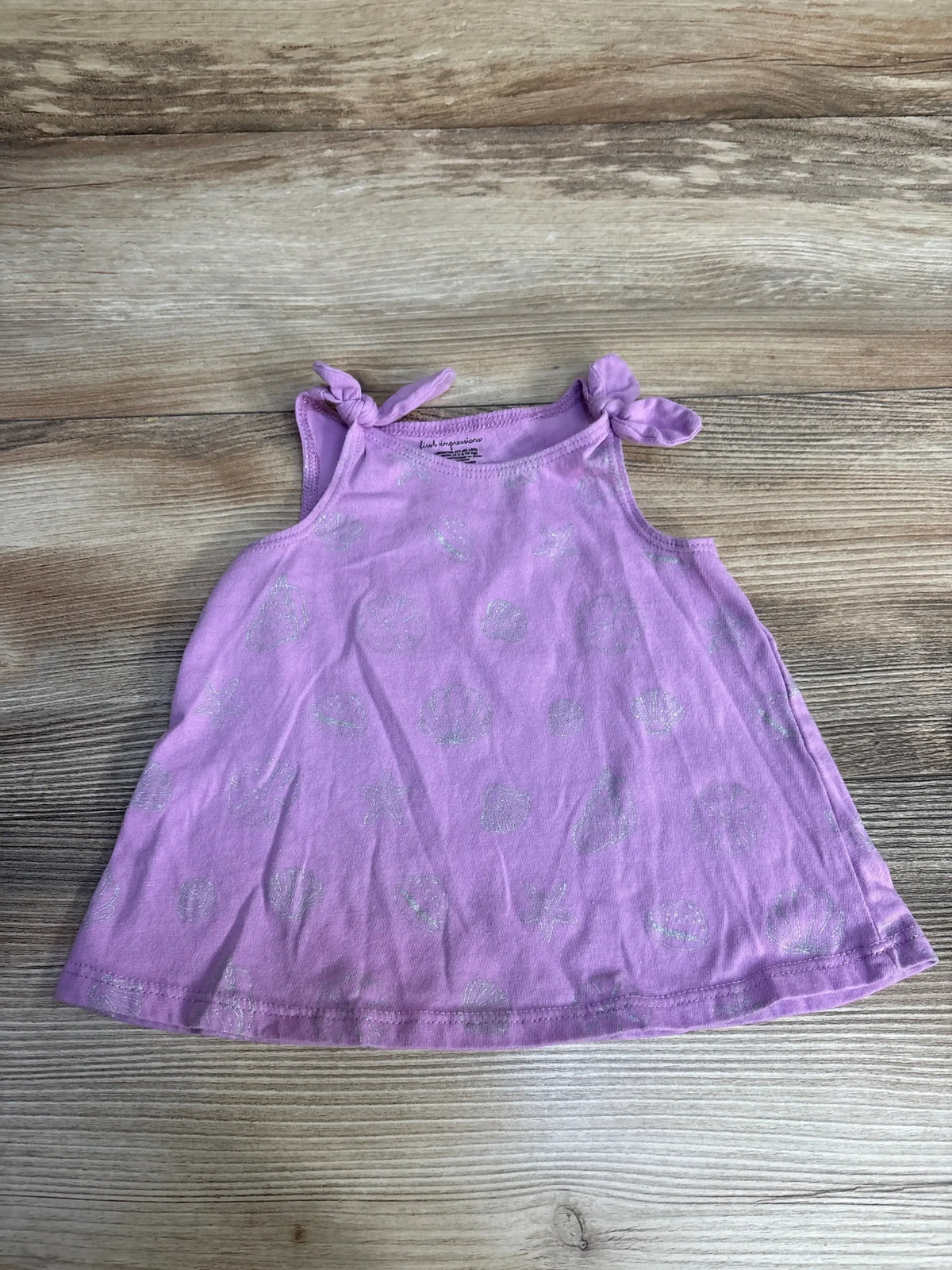 Flat lay of First Impressions seashell tank top in purple with silver print and knotted shoulder ties on wood background