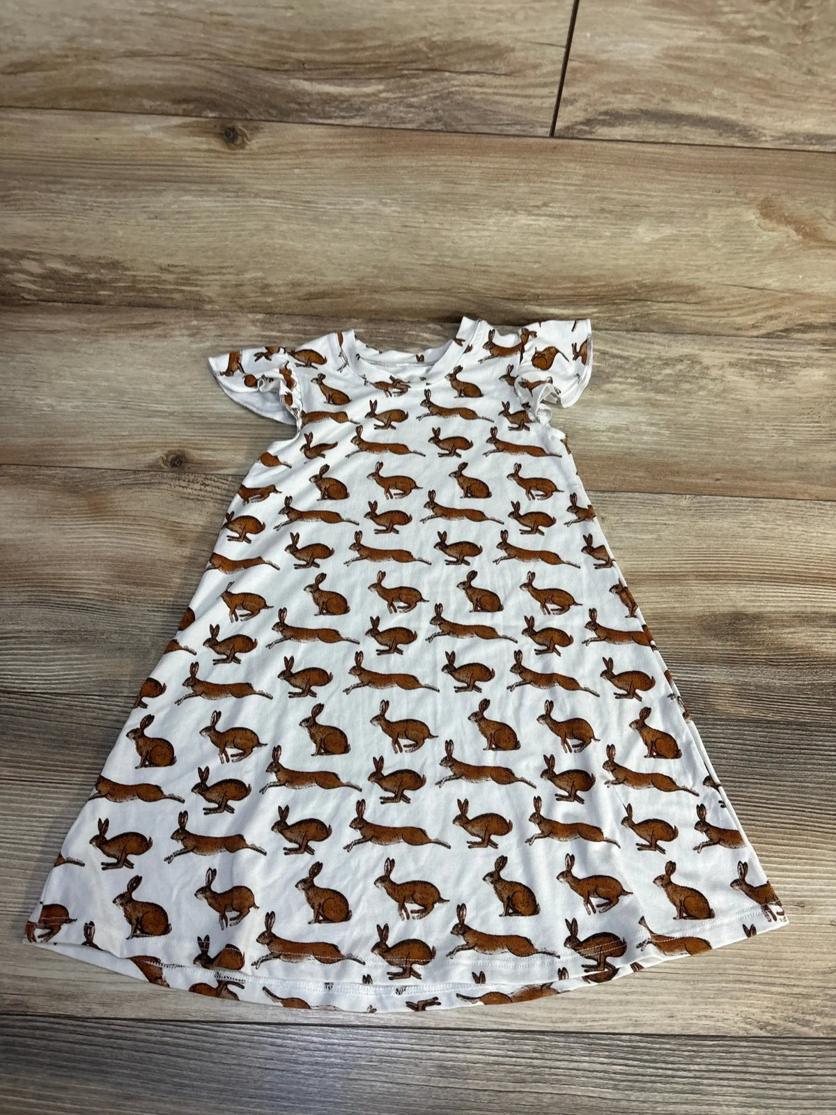 White short sleeve children's dress with brown bunny print, laid flat on wood surface