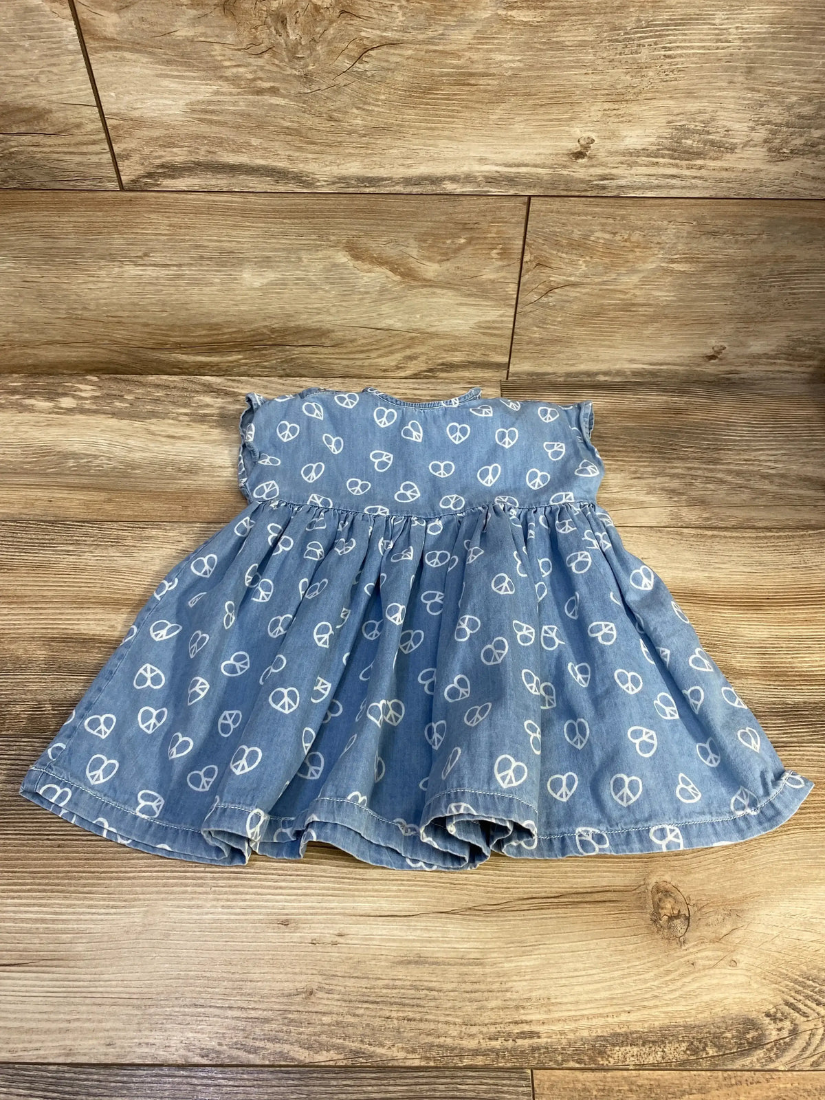 Flat lay of Molo Channi Love Peace dress, blue with white peace-heart print and ruffle cap sleeves on wooden background