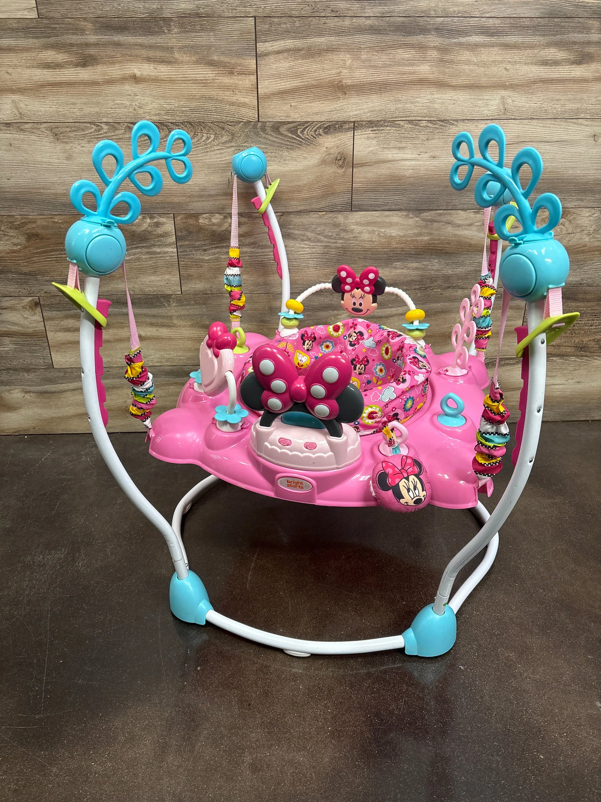 Front view of Disney Baby Minnie Mouse PeekABoo Activity Jumper with pink seat, hanging toys, and turquoise arches