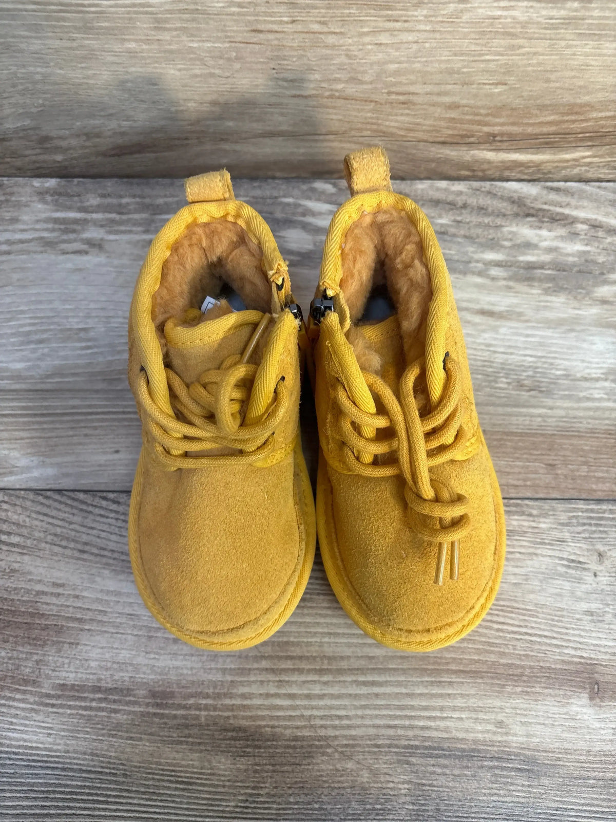Top-down view of Ugg Neumel II toddler boots size 8C in yellow suede with plush fur lining and laces on a wooden floor
