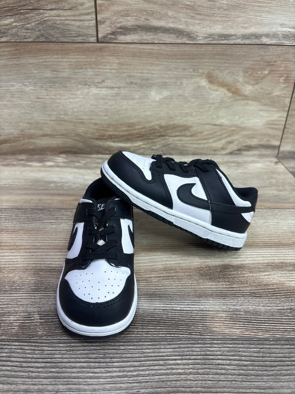 Pair of Nike Dunk Low TD 'Black White' toddler sneakers on a wooden surface.