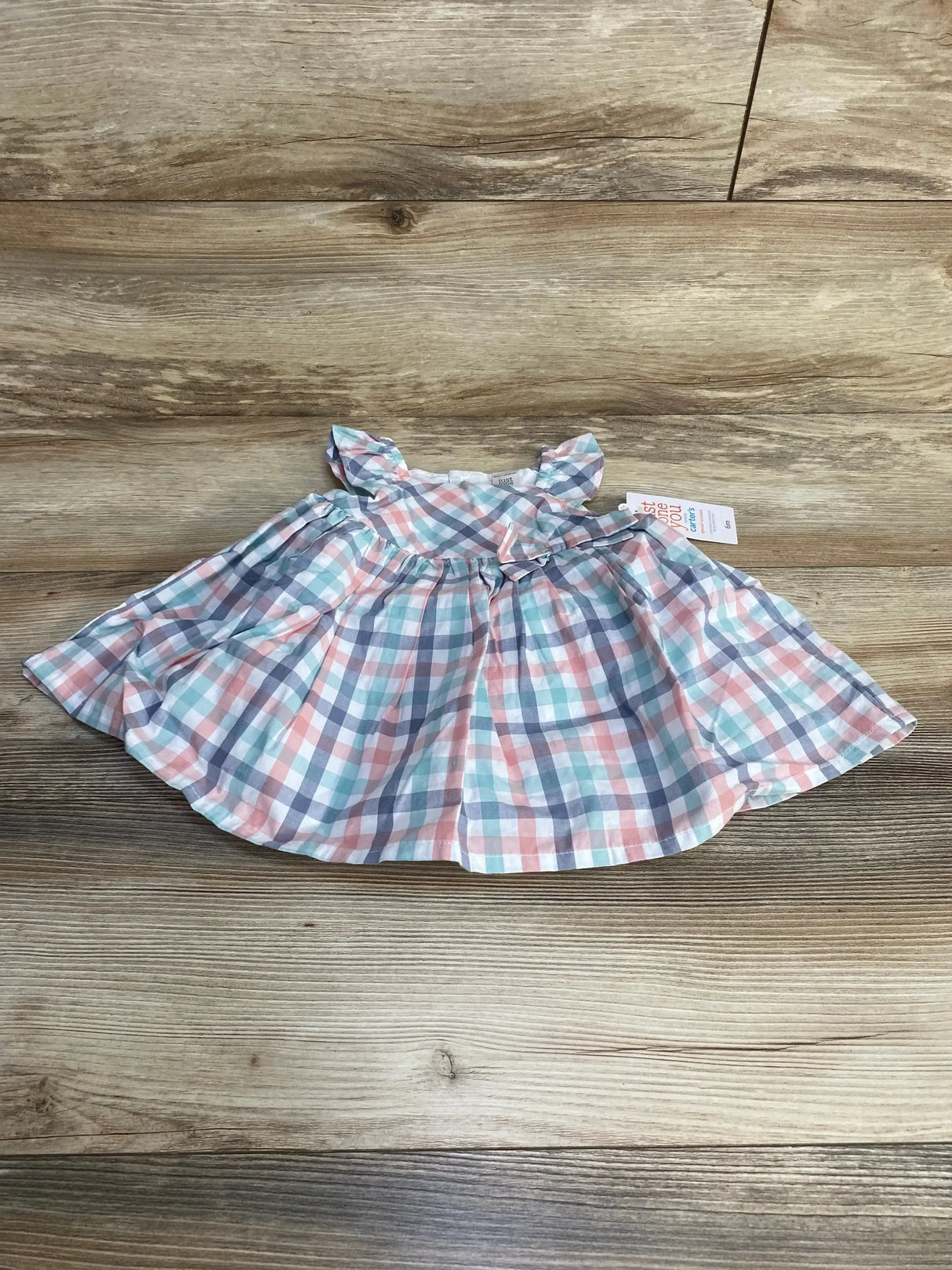 Flat lay of infant pastel plaid dress and bloomers showcasing ruffled cap sleeves and gathered skirt on wood background