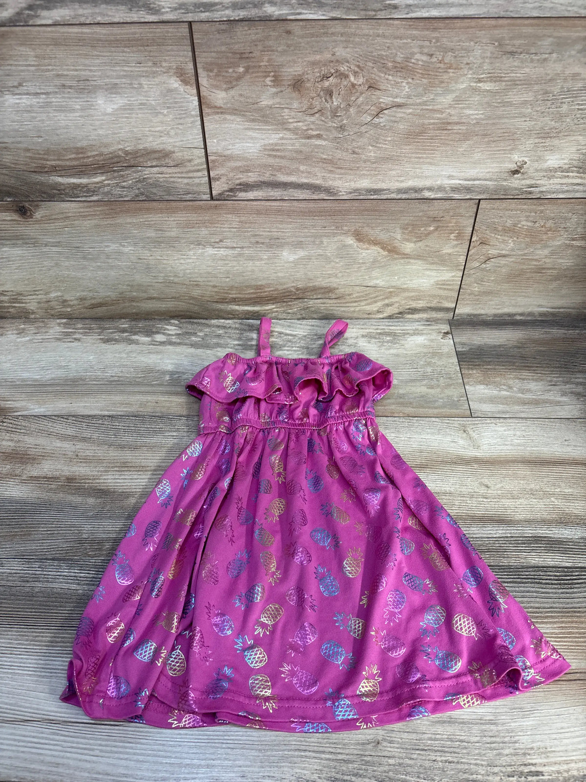 Front view of Picapino pineapple dress showcasing purple fabric, ruffled neckline, and multicolor pineapple print on wood-look flooring