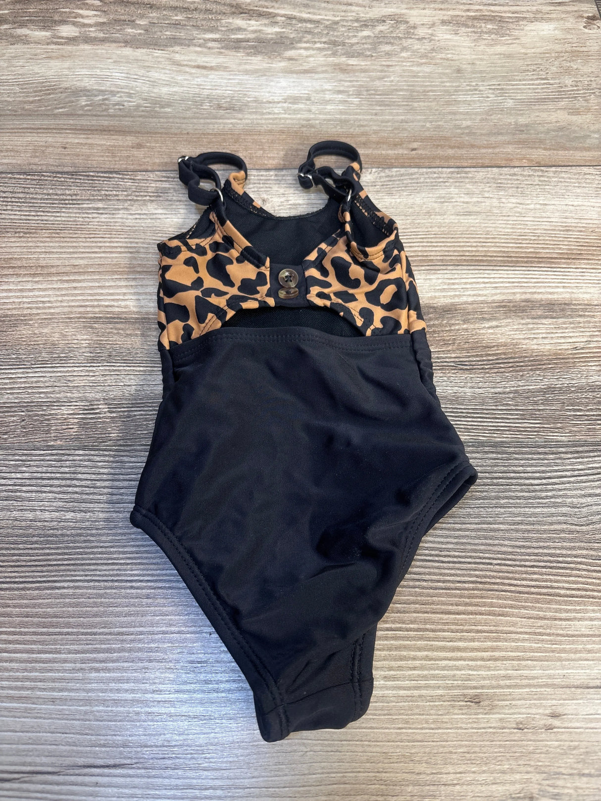 Kids black one-piece swimsuit with leopard print straps and button detail on wood background