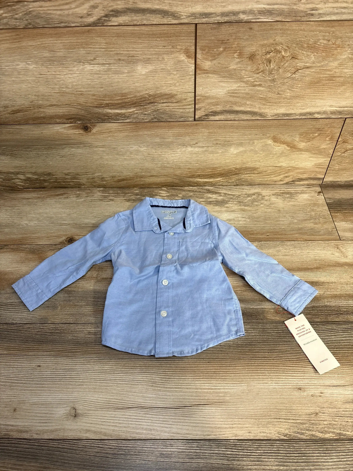 Light blue toddler button-up shirt with long sleeves on wood floor, retail tag attached
