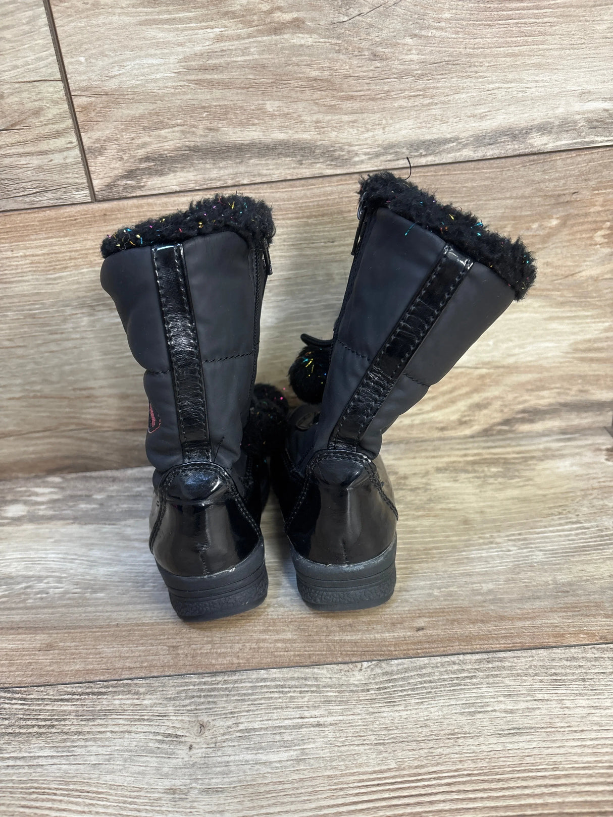 Rear view of Totes Sweetheart toddler winter boots size 6C showing black faux-fur trim, patent heel and pom-pom on wooden floor