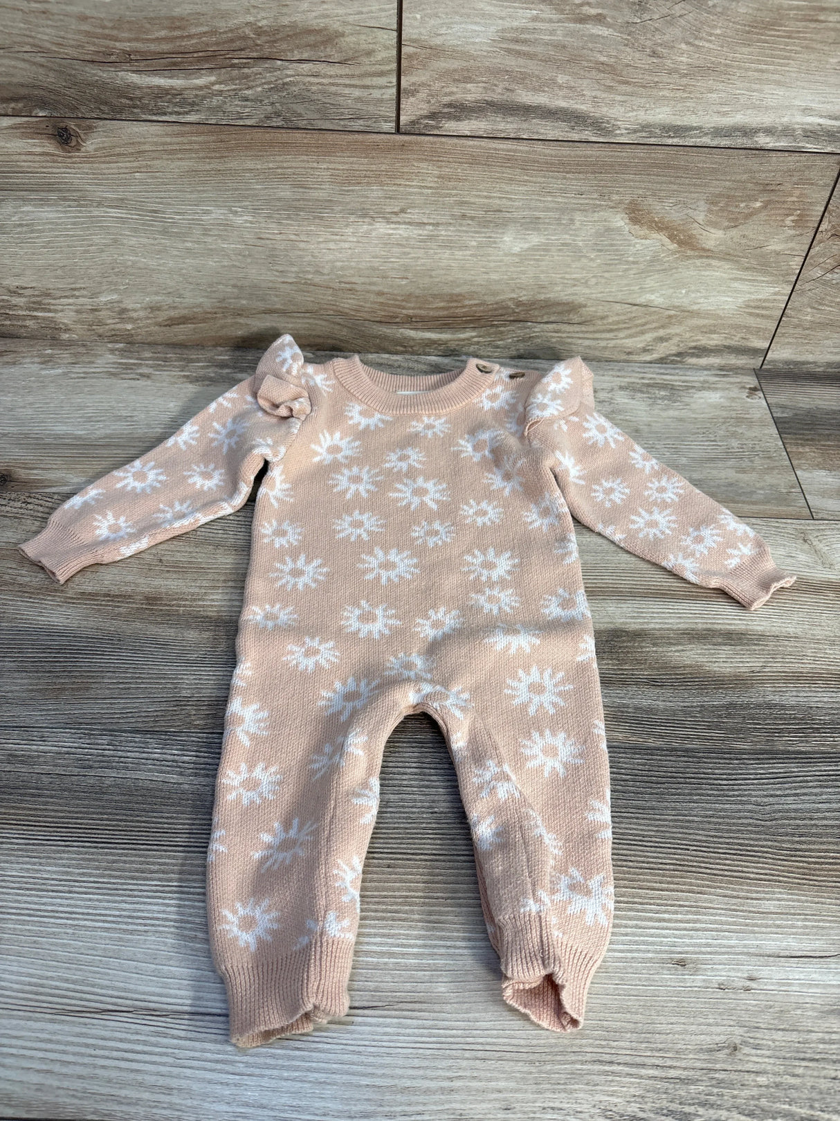 Flat lay of Luna + Luca Classic Organic Ruffle Jumpsuit in peach showcasing ruffle sleeves and white floral print on wood floor