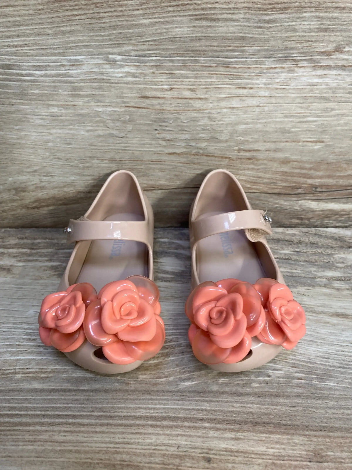 Three-quarter view of Mini Melissa Ultragirl flats in beige and pink with flower detail and glossy jelly finish