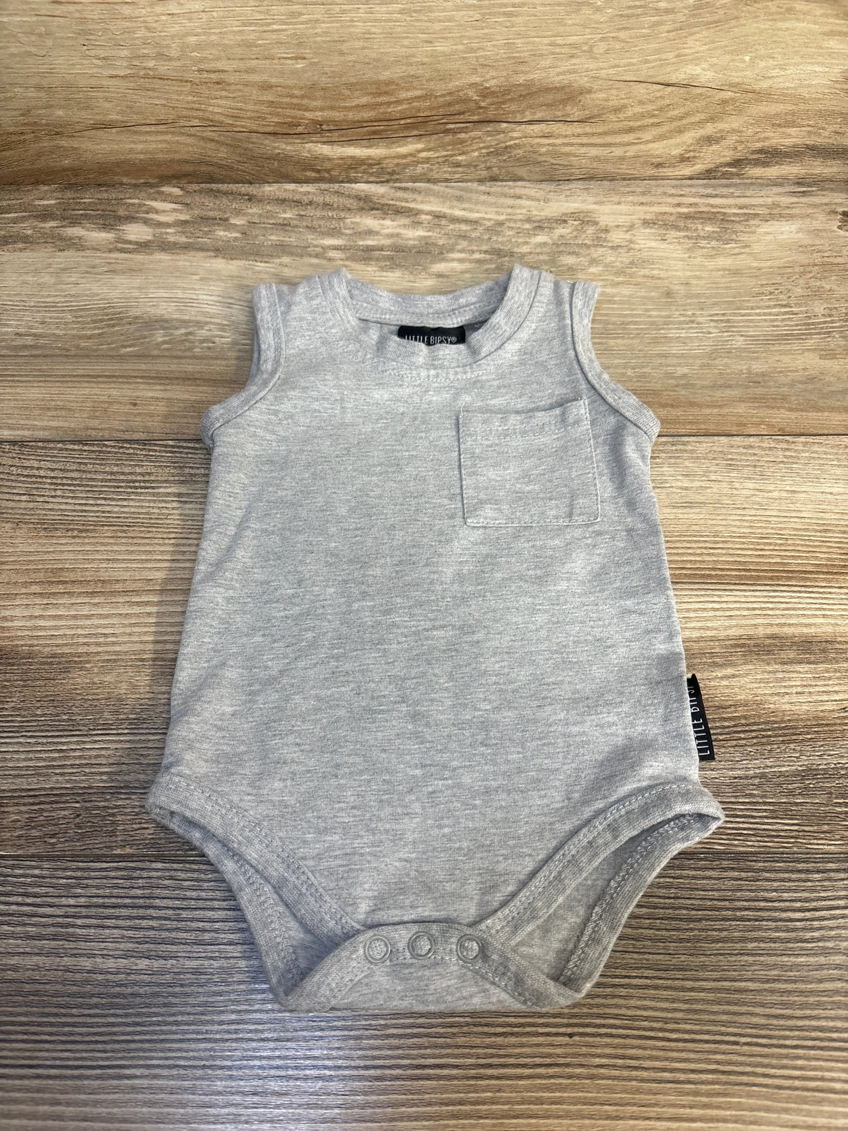 Gray sleeveless baby bodysuit with front pocket and snap closure, laid on wooden surface