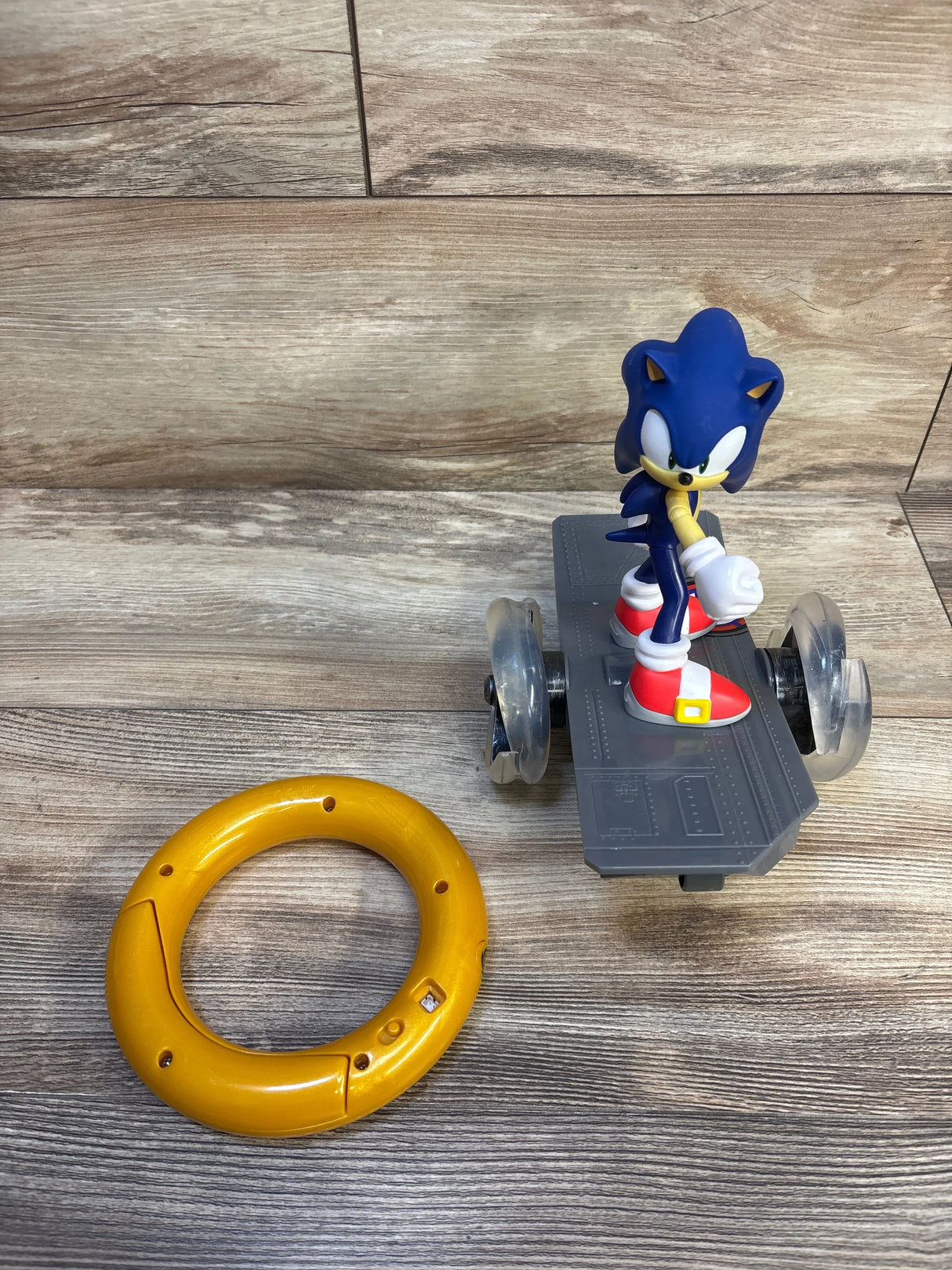 Sonic the Hedgehog toy on a gray skateboard with plastic ring on wooden background