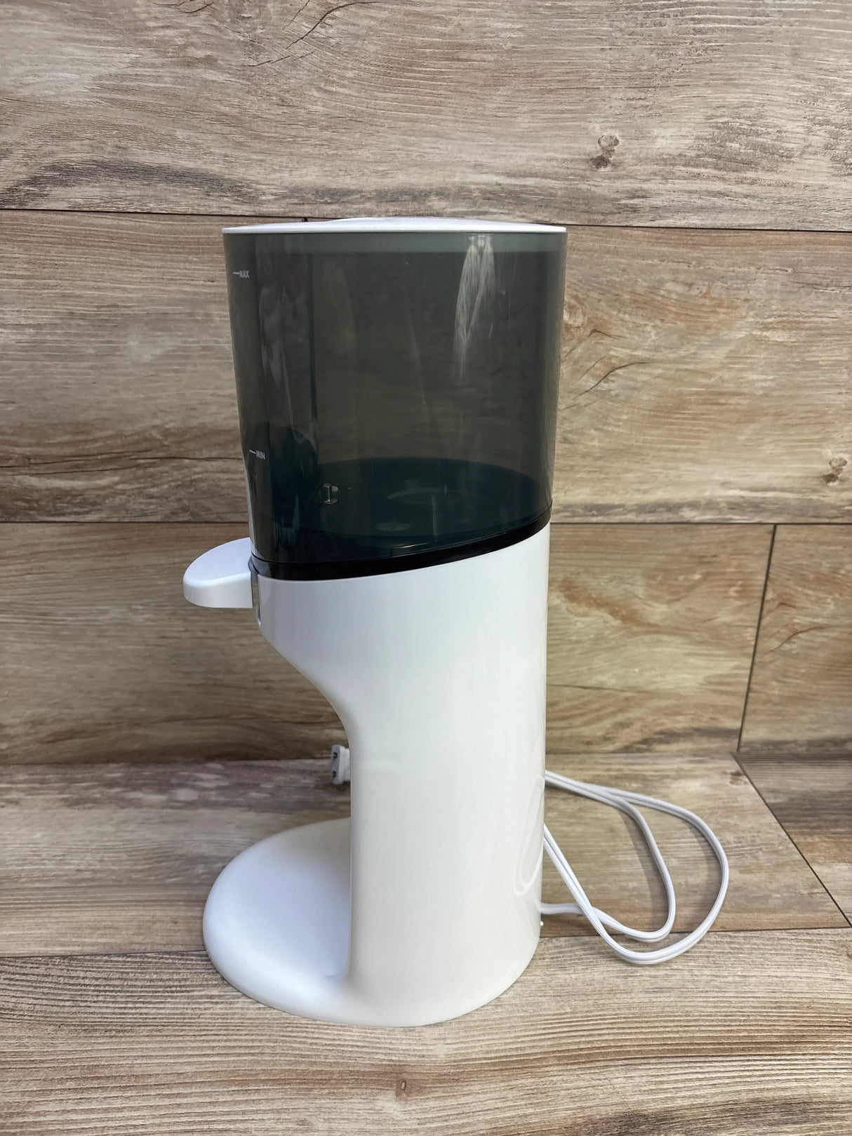 Three-quarter view of Baby Brezza Instant Bottle Warmer showing white body, dark reservoir, and power cord on wood planks
