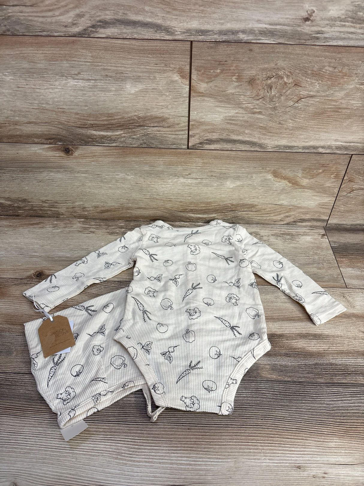 Long sleeve baby bodysuit with vegetable print, laid on rustic wood floor