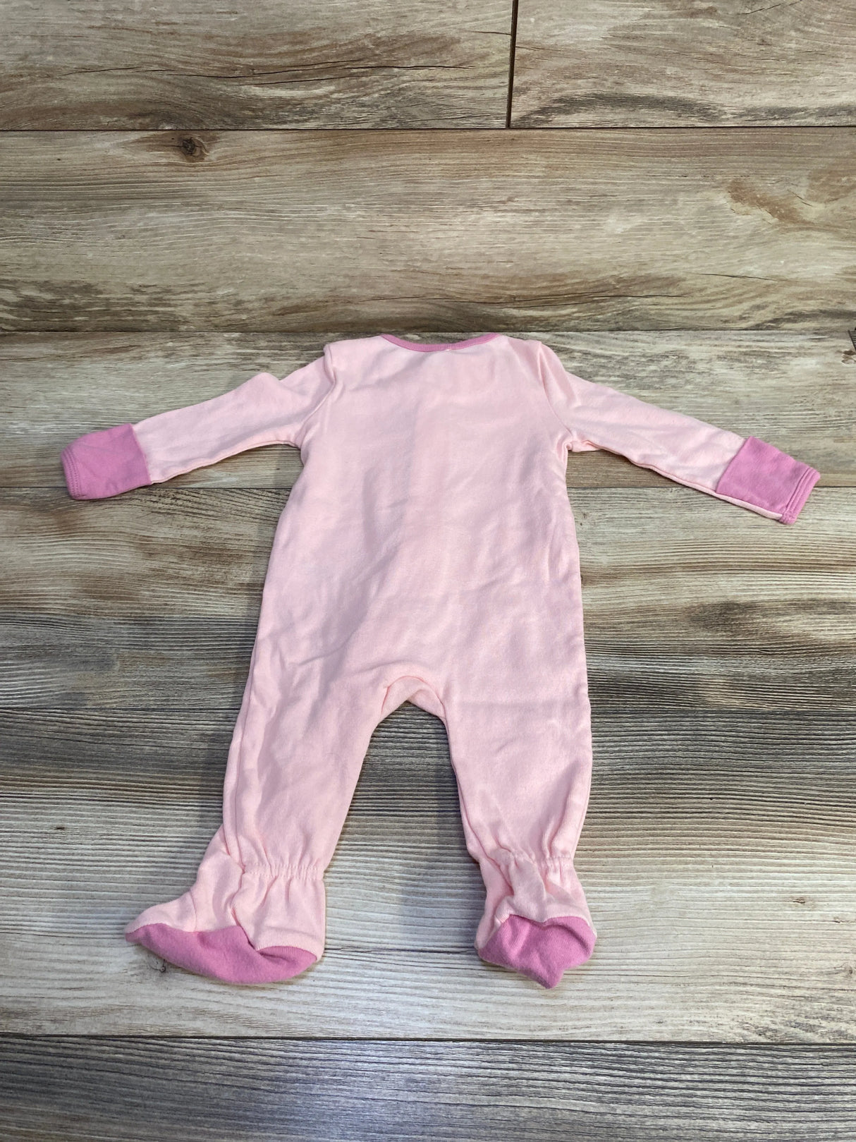 Back view of a pink baby onesie with long sleeves and footed legs on wooden floor