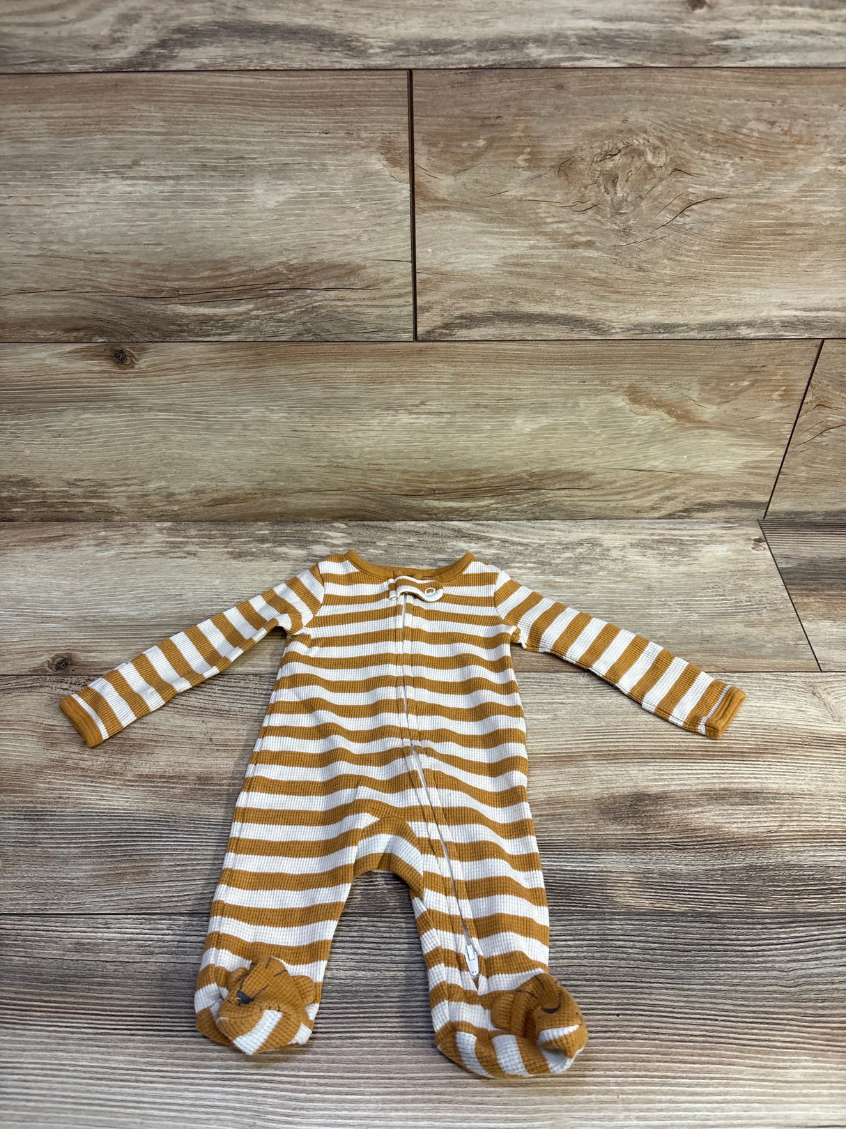 Flat lay of Just One You newborn waffle knit sleeper showing mustard and white stripes and front zipper on wood background