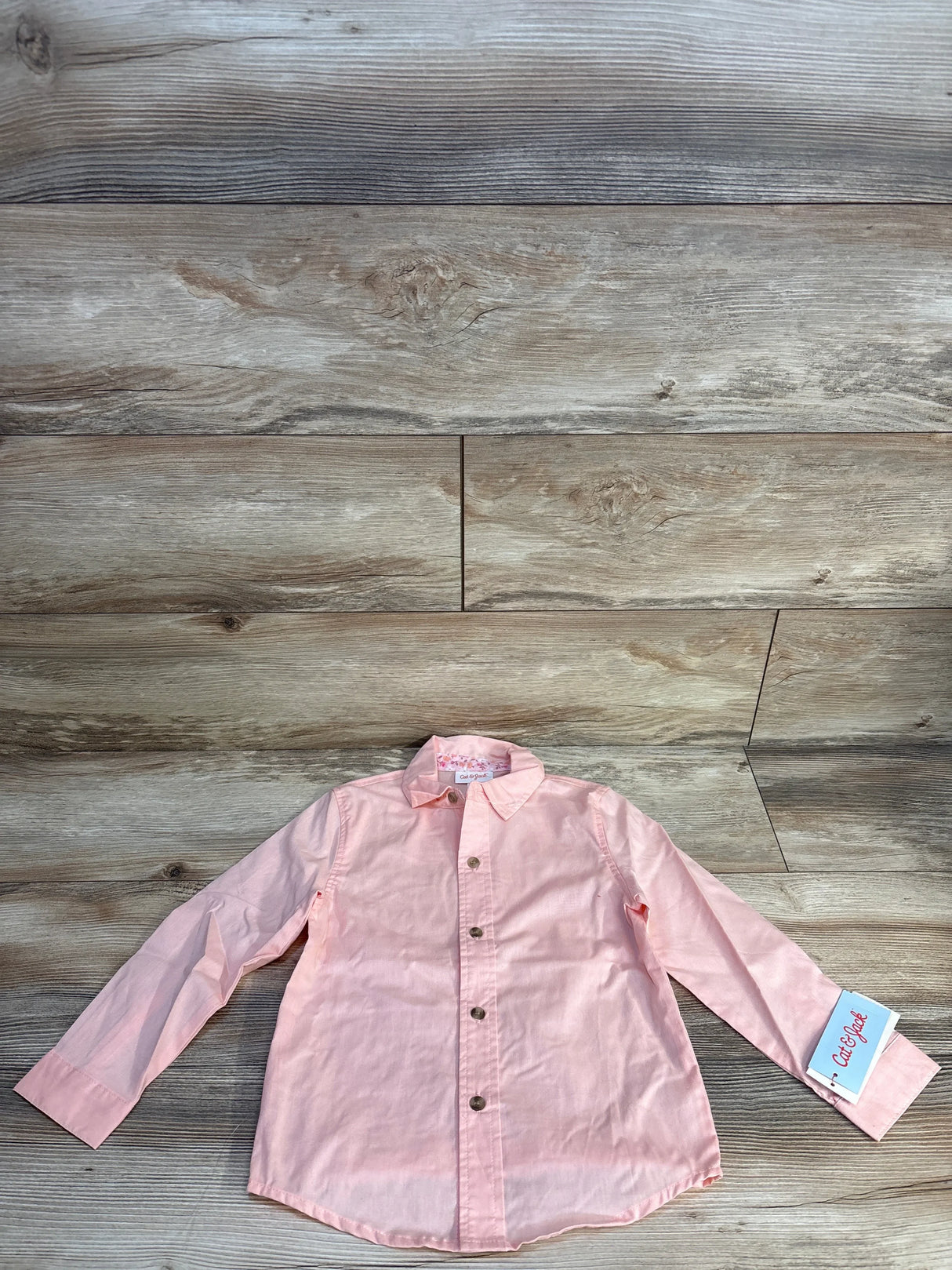 Light pink long sleeve kids button-up shirt with tag on wood background