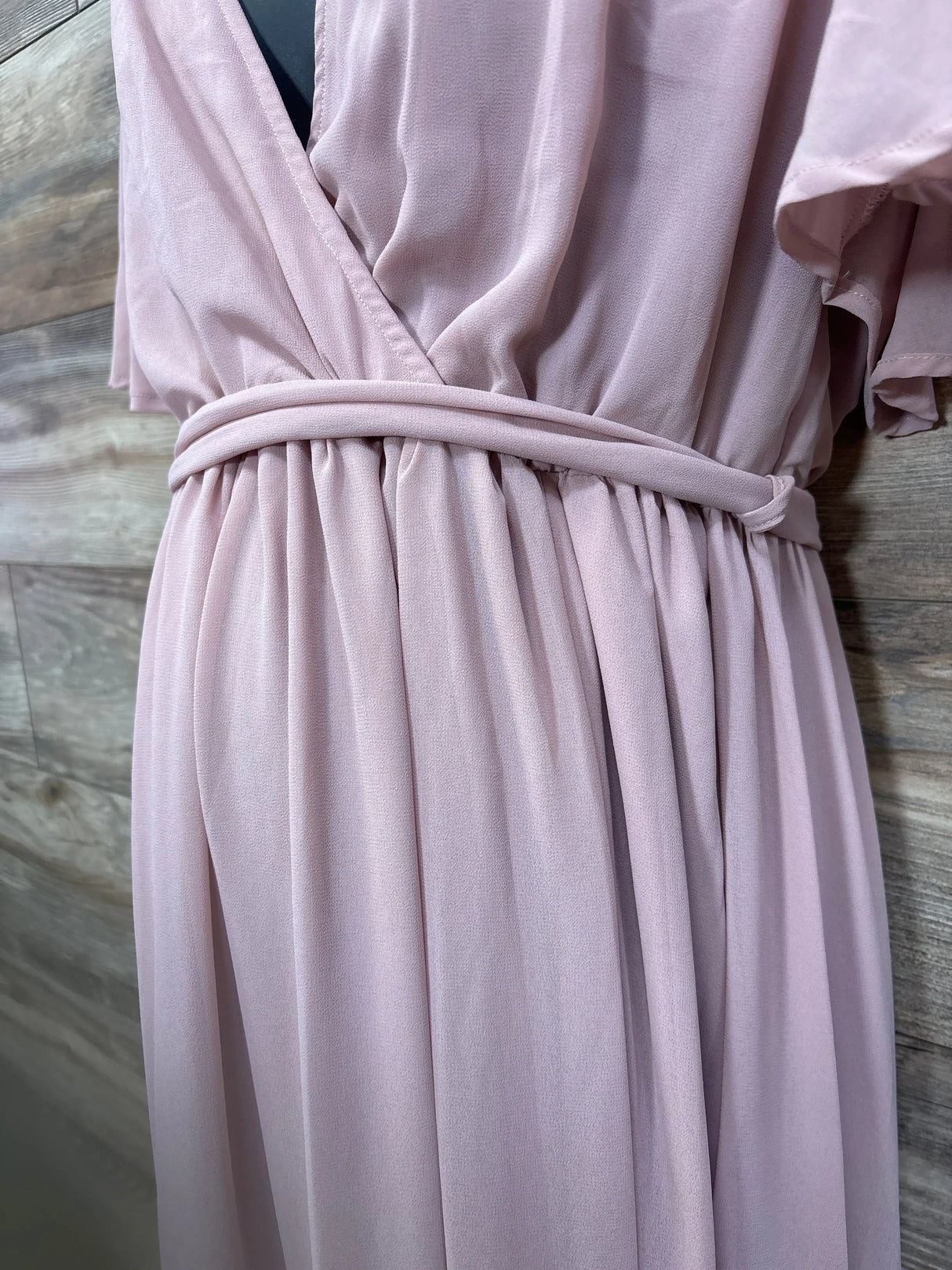 Close-up of blush Baltic Born maternity maxi dress showing gathered waist and fabric-covered belt with wood background