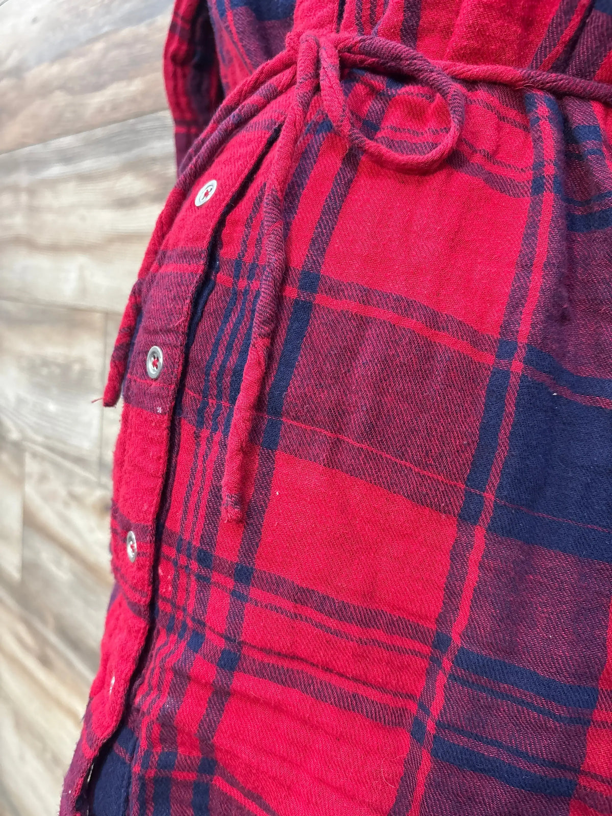 Red and navy plaid flannel shirt with waist tie detail, close-up view