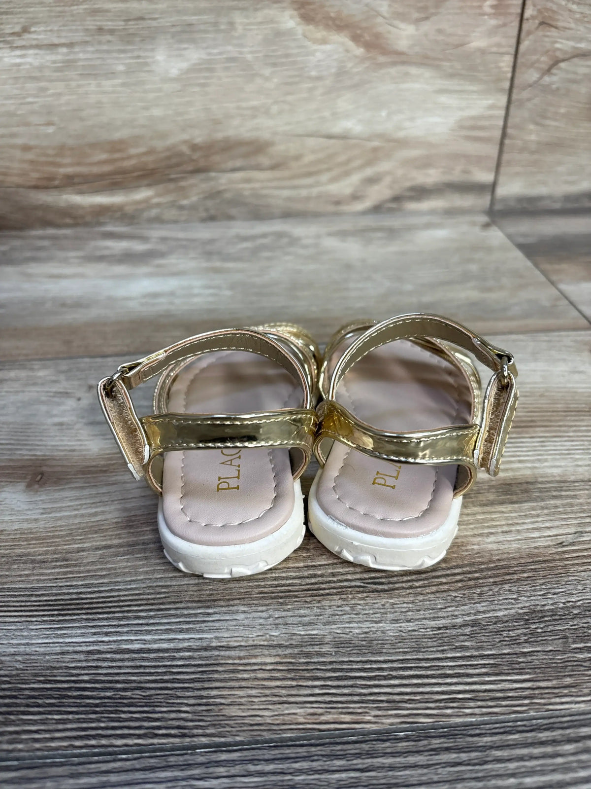 Children's Place metallic gold sandals for toddlers on a wooden floor