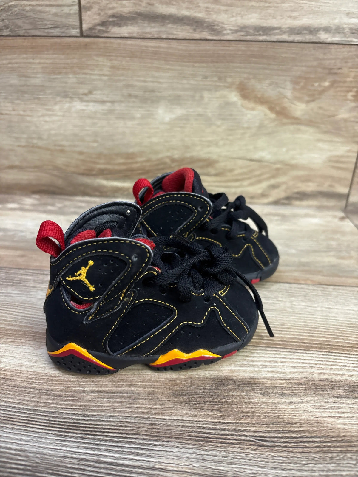 Front view of Air Jordan 7 Retro TD Citrus sneakers size 4C showcasing black uppers, red lining, and yellow accents on wood flooring