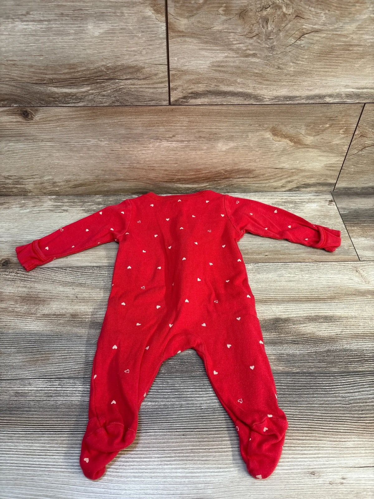 Red baby sleeper with white heart print, long sleeves and footed design on wood floor