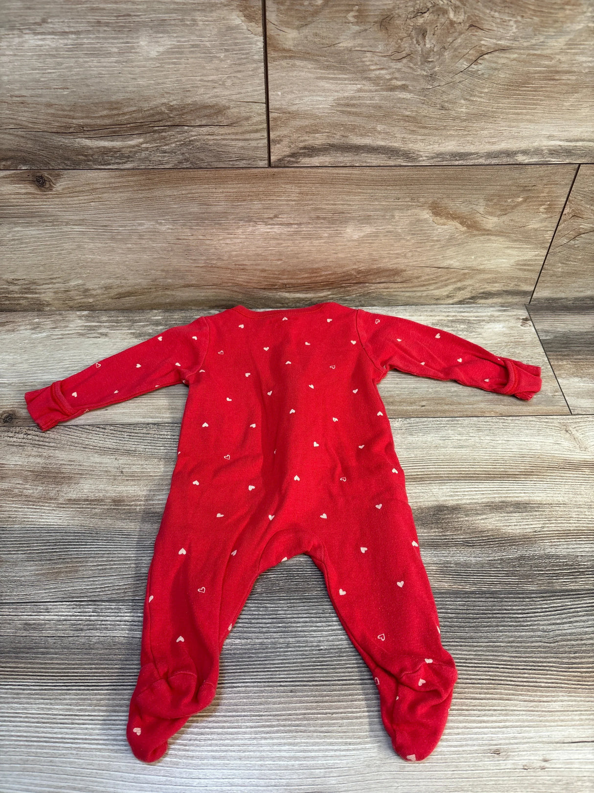 Red baby sleeper with white heart print, long sleeves and footed design on wood floor