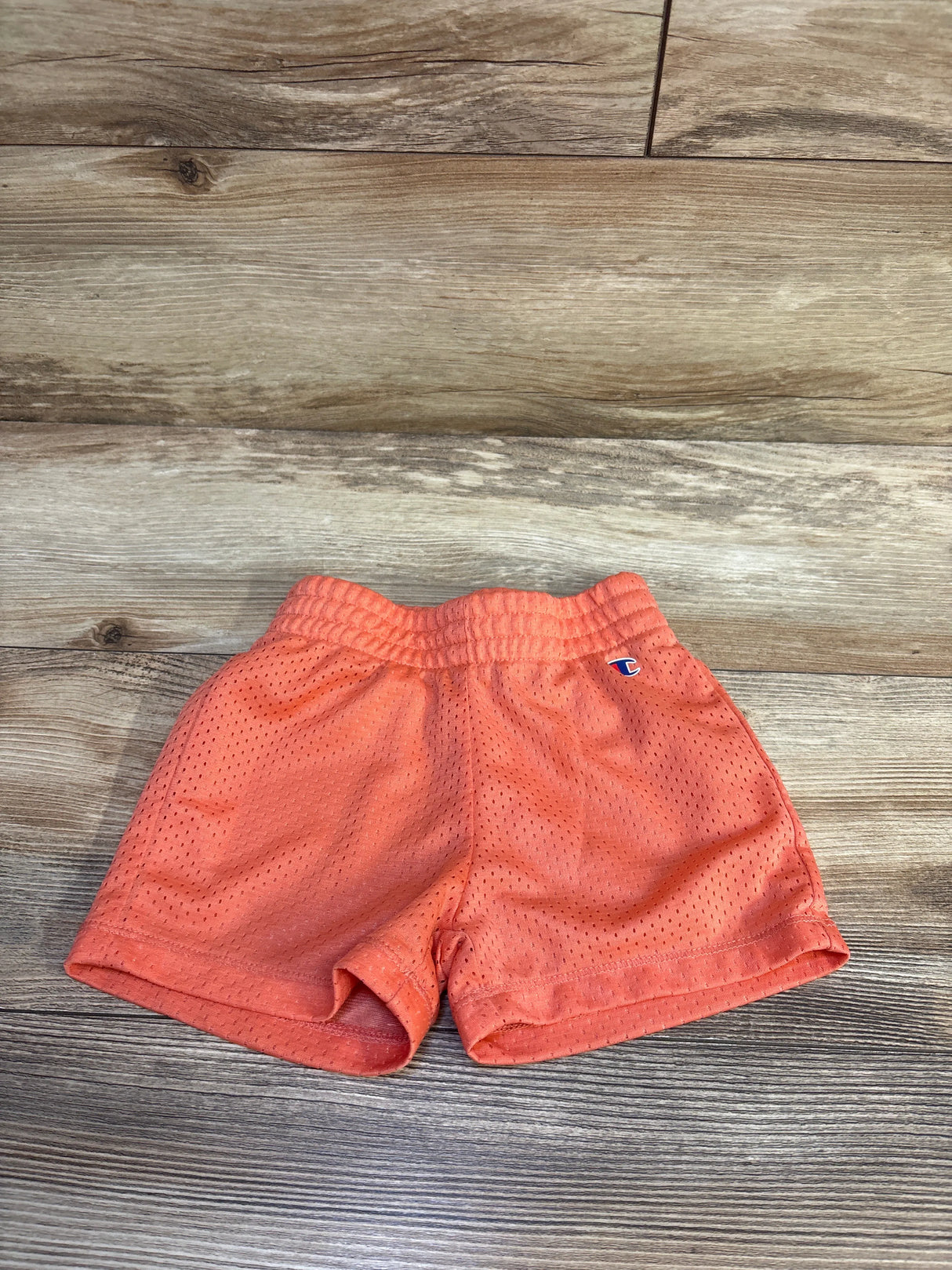 Flat lay of coral Champion toddler mesh shorts showcasing elastic waistband and small logo on wood background