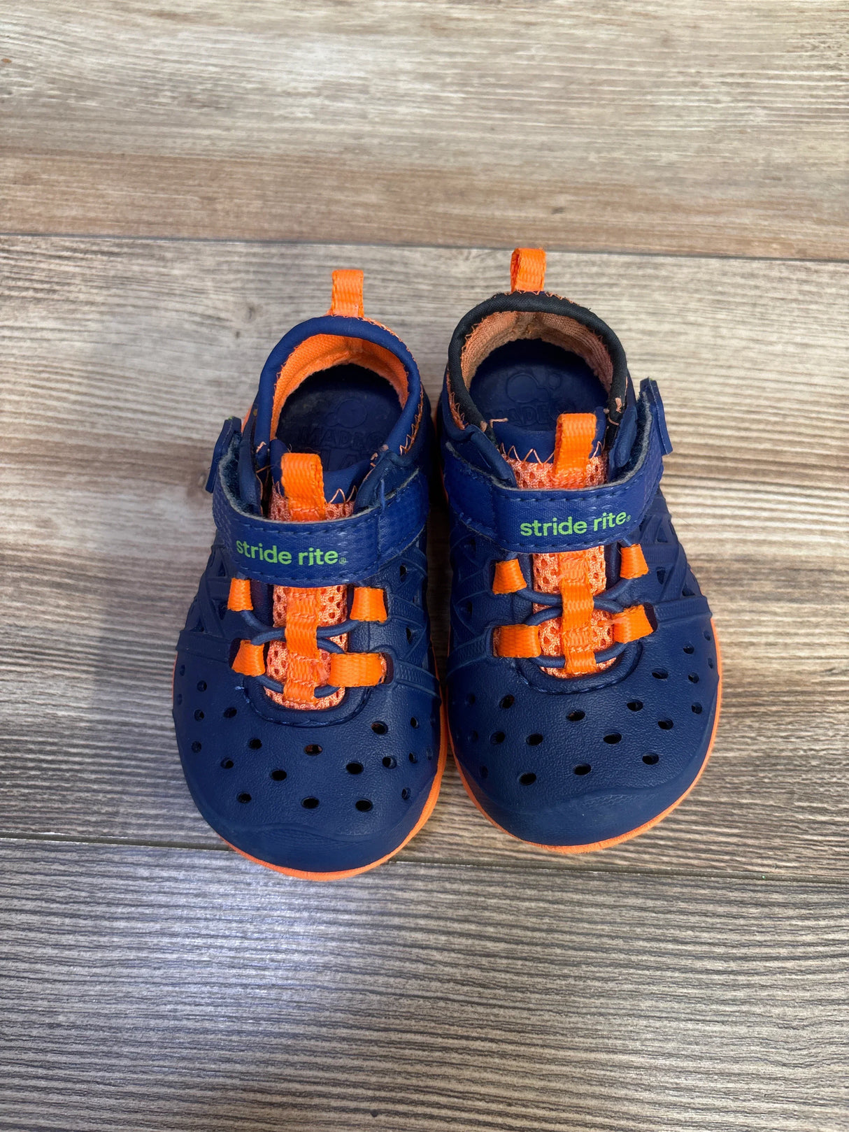 Top view of navy and orange Stride Rite Phibian water shoes showing perforated toes, bungee laces and velcro strap on wood