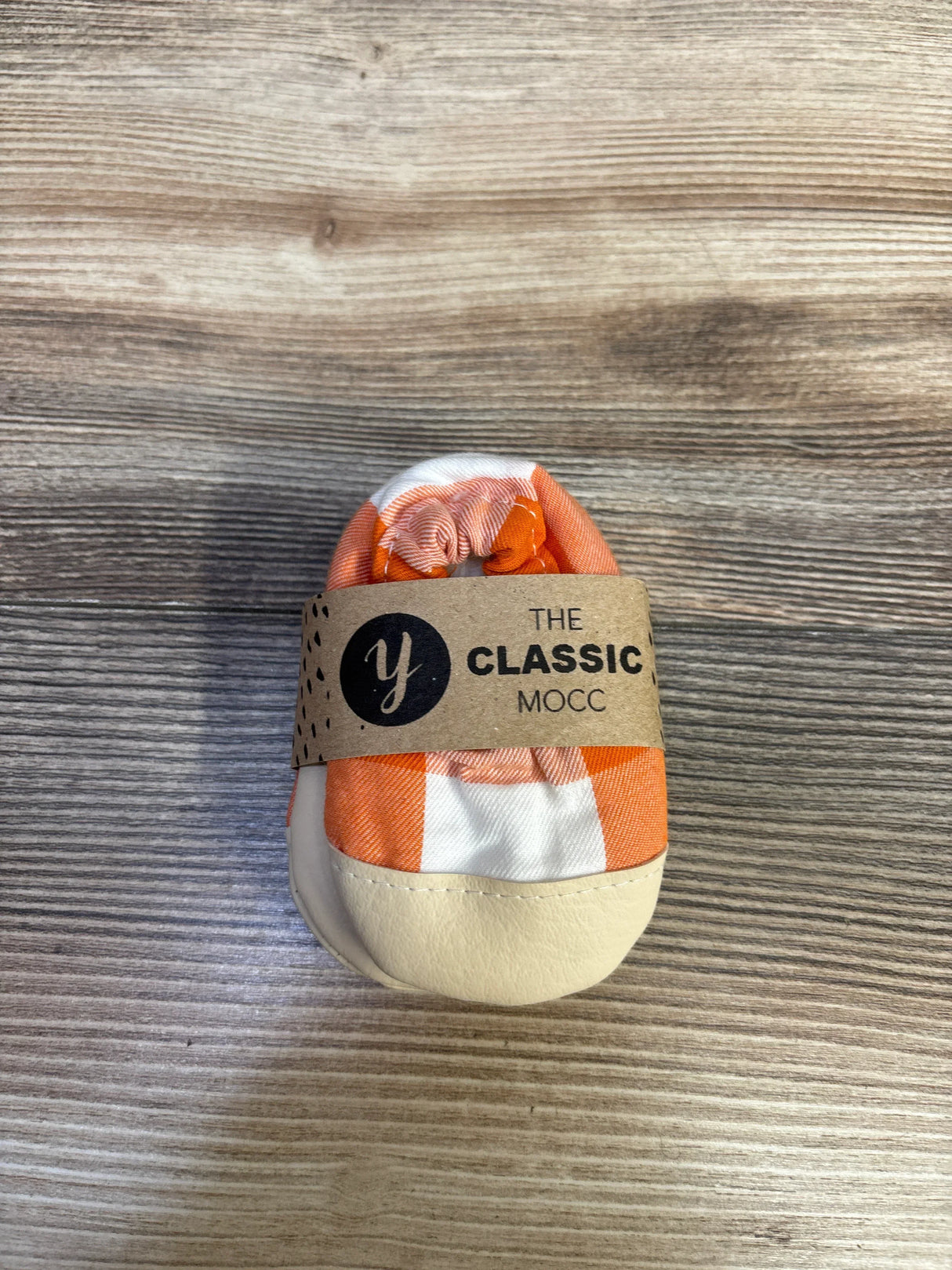 Front view of NEW Yeti Moccs The Classic Mocc soft sole shoe showcasing orange and cream design on a wood grain background