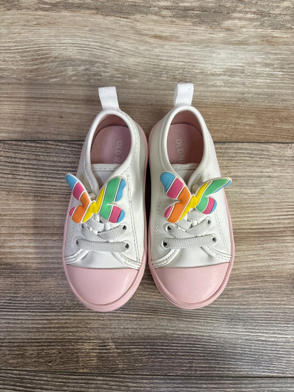 White toddler shoes with pink toe caps and colorful butterfly decorations on wooden floor