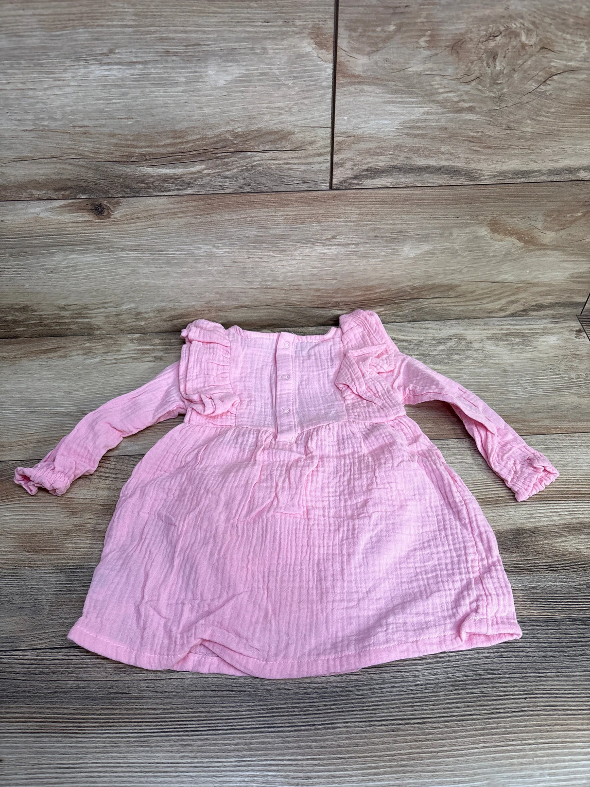 Pink long sleeve baby dress with ruffle details on wood background