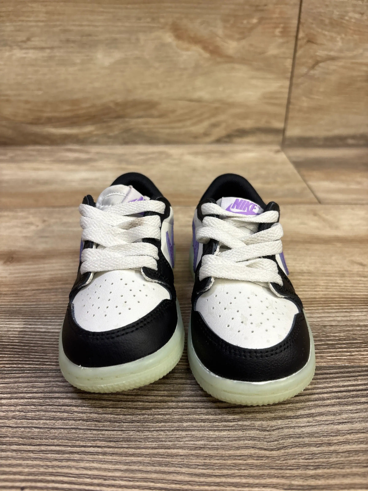 Front view of Air Jordan 1 Retro Low OG TD Black Raspberry sneakers showing black and white uppers, purple accents on wood flooring