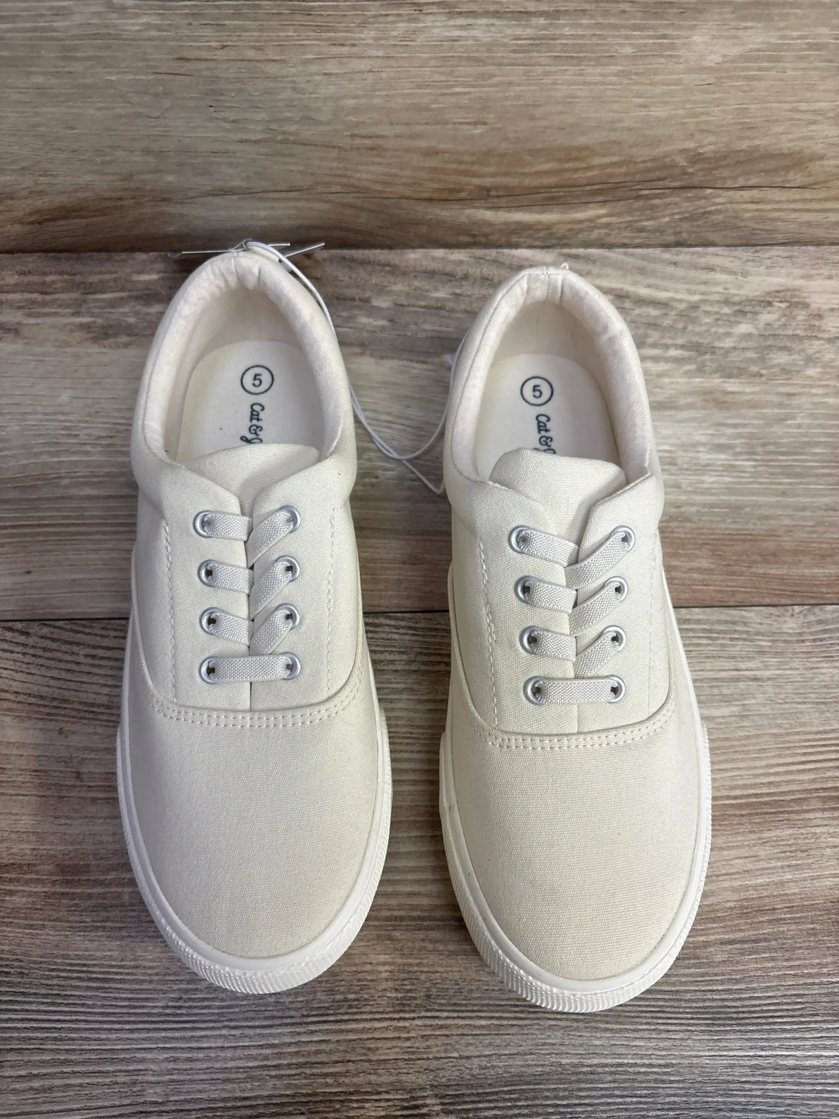 Angled side view of Cat & Jack off-white slip-on kids sneakers size 5Y with canvas upper and rubber sole on wood