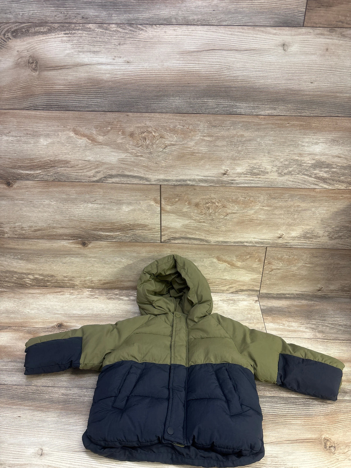 Front view of Zara colorblock hooded puffer jacket showcasing green and navy color blocking, hood, and pockets on wood flooring