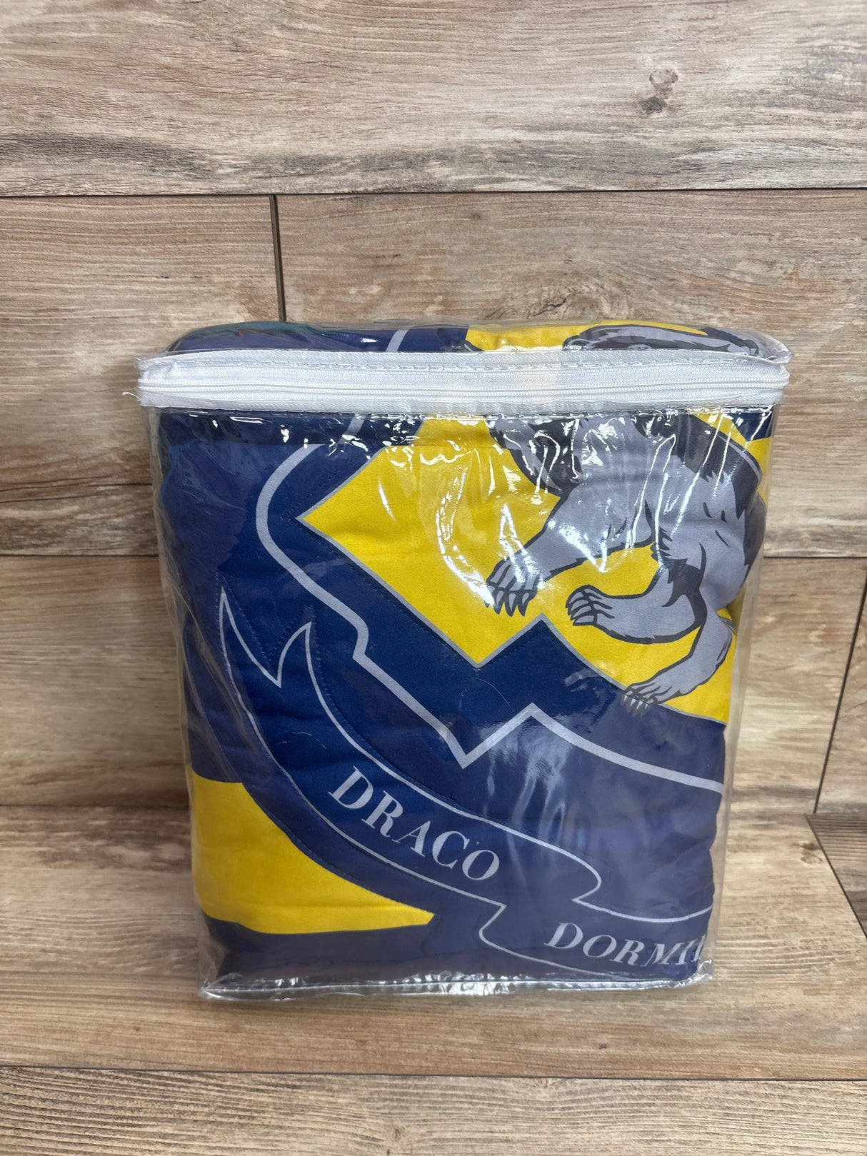 Folded NoJo Harry Potter 4pc toddler bed set in clear zip bag showing blue and yellow crest and DRACO text on wooden background