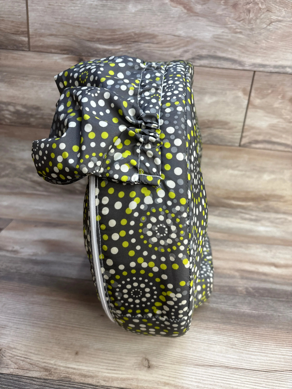 Side view of My Brest Friend nursing pillow with gray fabric and white-lime dot fireworks pattern, zipper on wood background