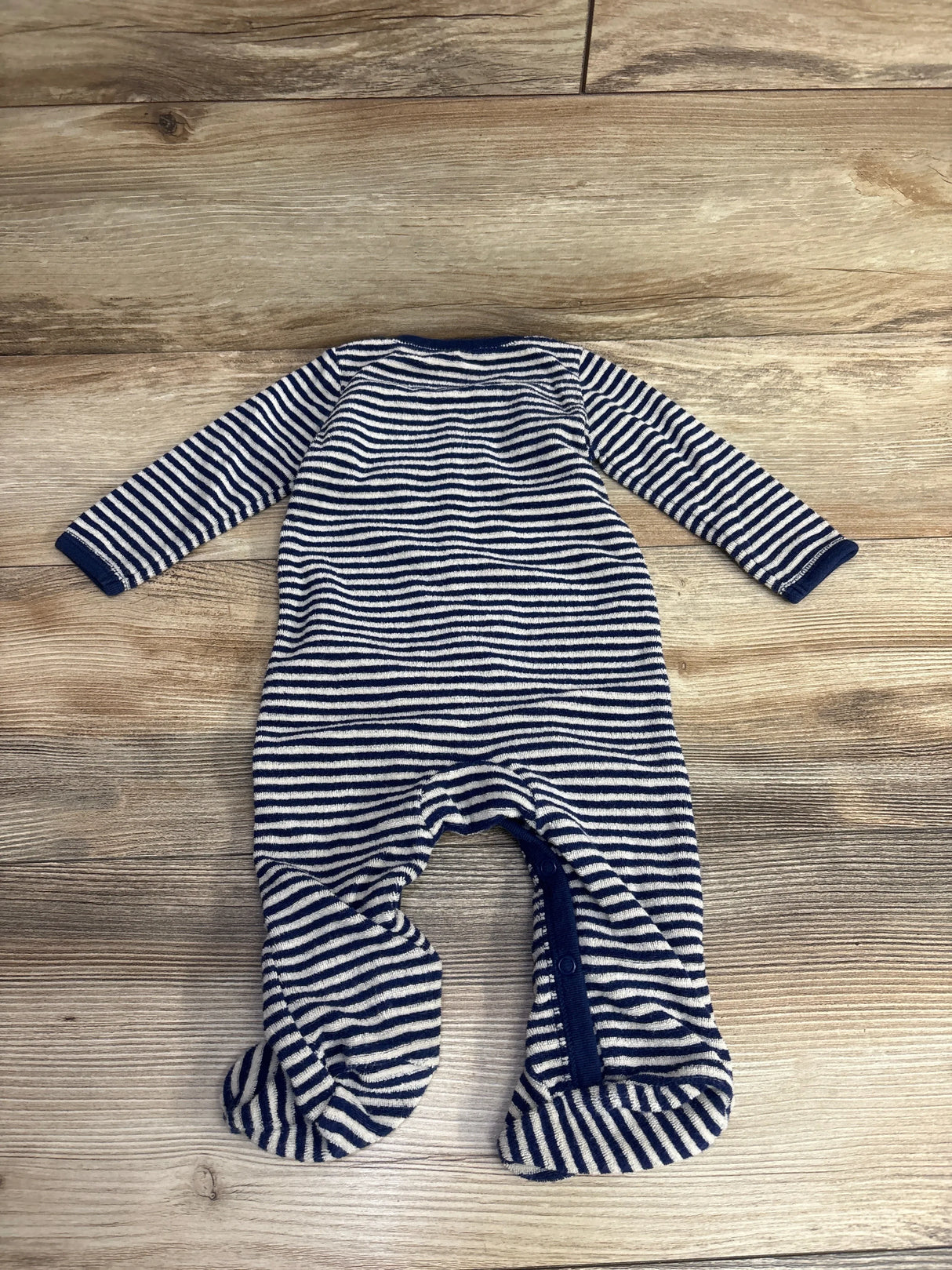 Striped navy blue and white long-sleeve infant onesie with footies on wooden floor