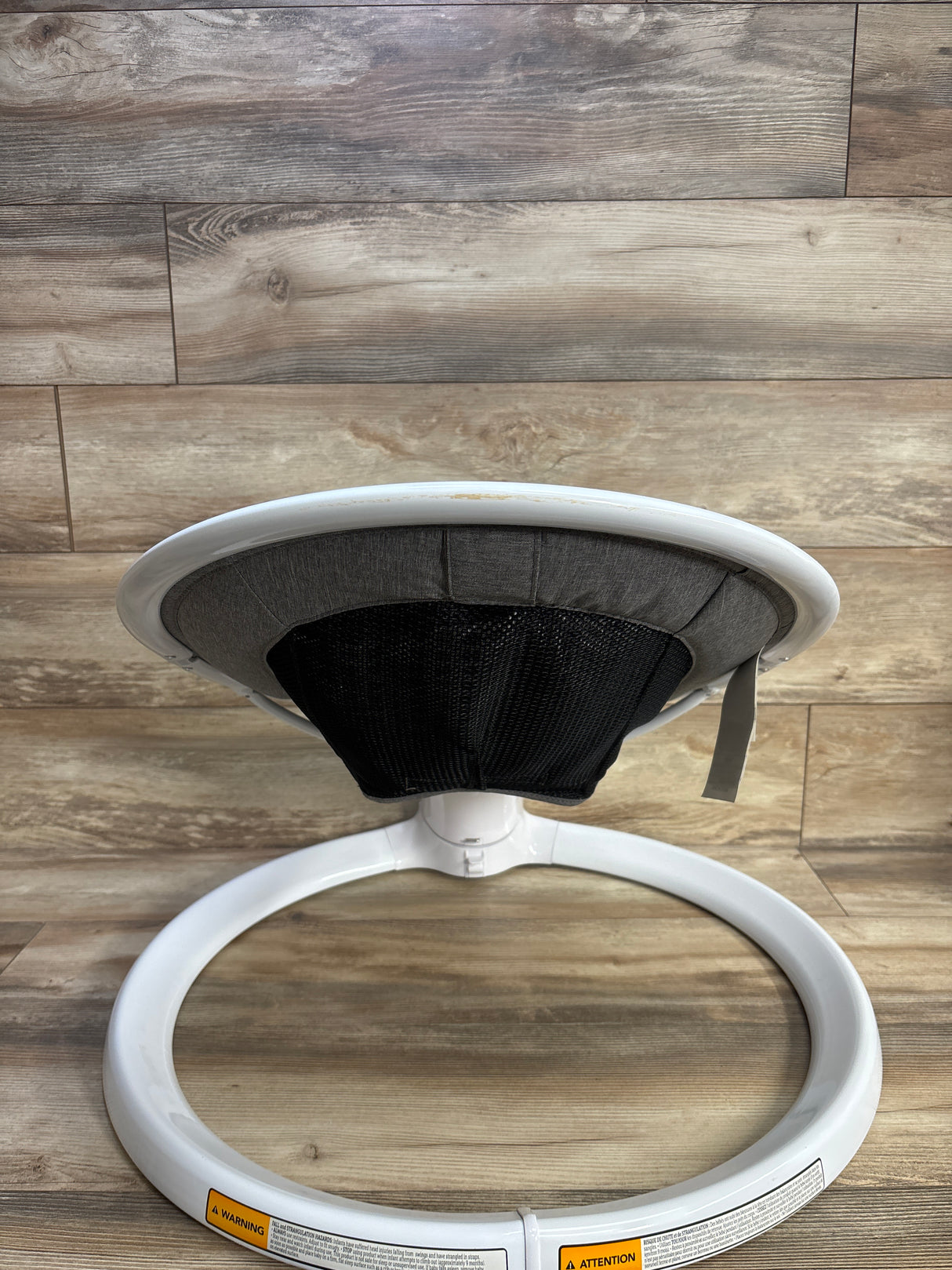 Rear view of Munchkin Bluetooth Enabled Baby Swing with white ring base, gray seat and black mesh back on wood floor