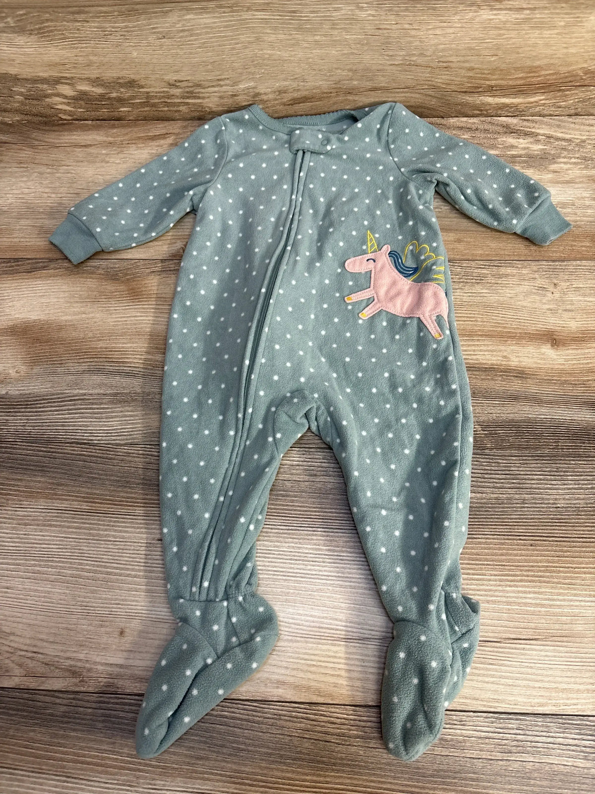 Flat lay of green Carter's polka dot footed sleeper showing front zipper, white dots and pink unicorn patch on wood