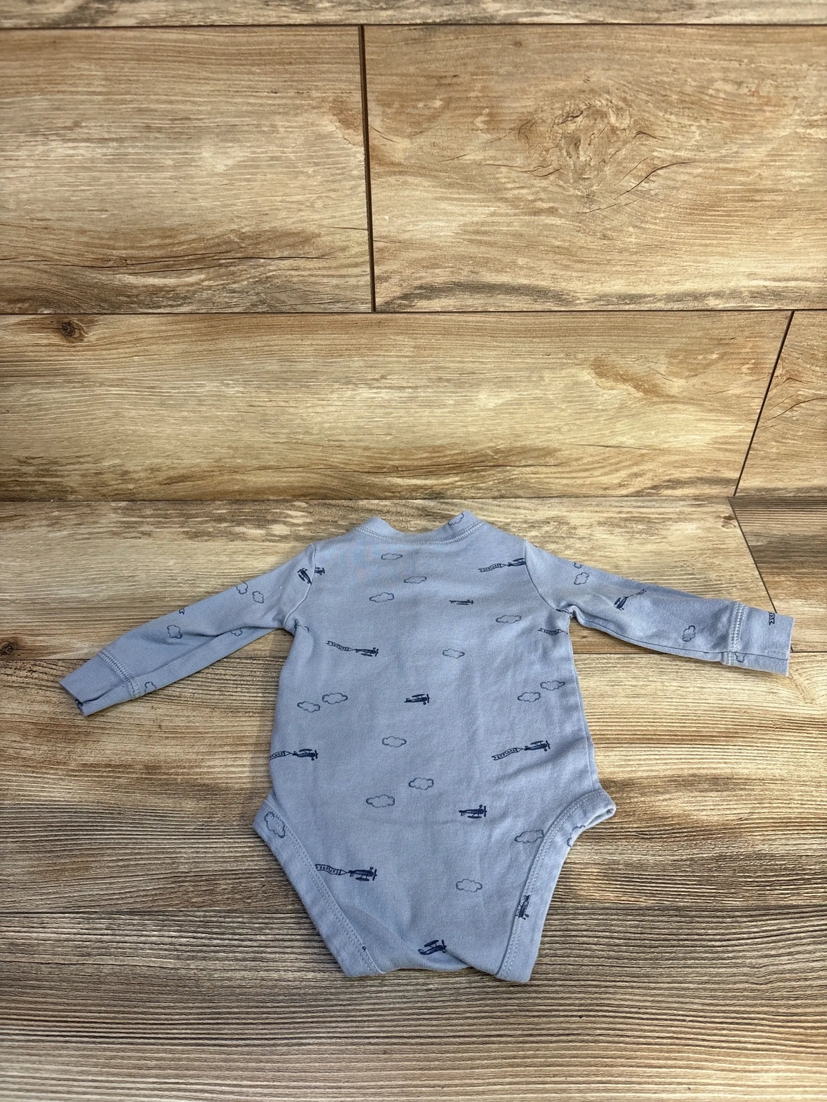 Front view of Just One You blue henley bodysuit in size 6 months showcasing cloud and airplane print on a wood background