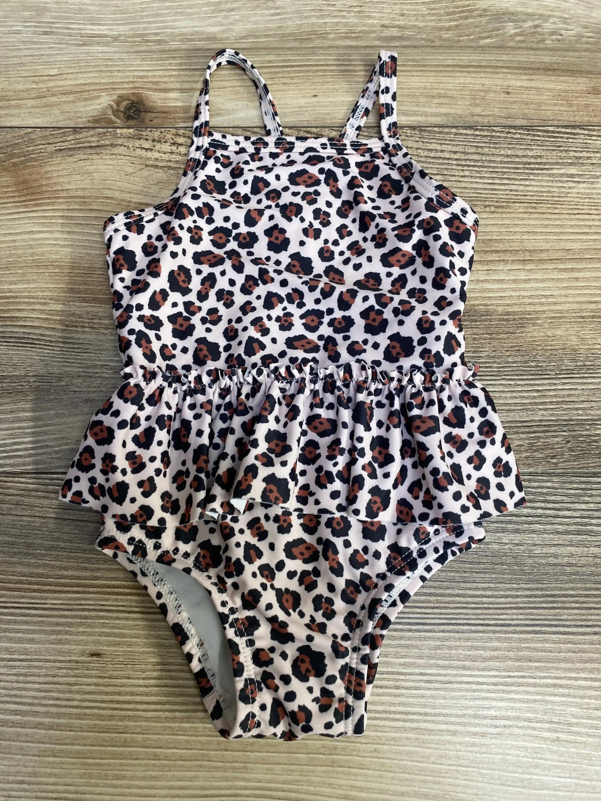 Flat lay of pink Cotton On newborn leopard-print one-piece swimsuit showing ruffle peplum and thin shoulder straps on wood background